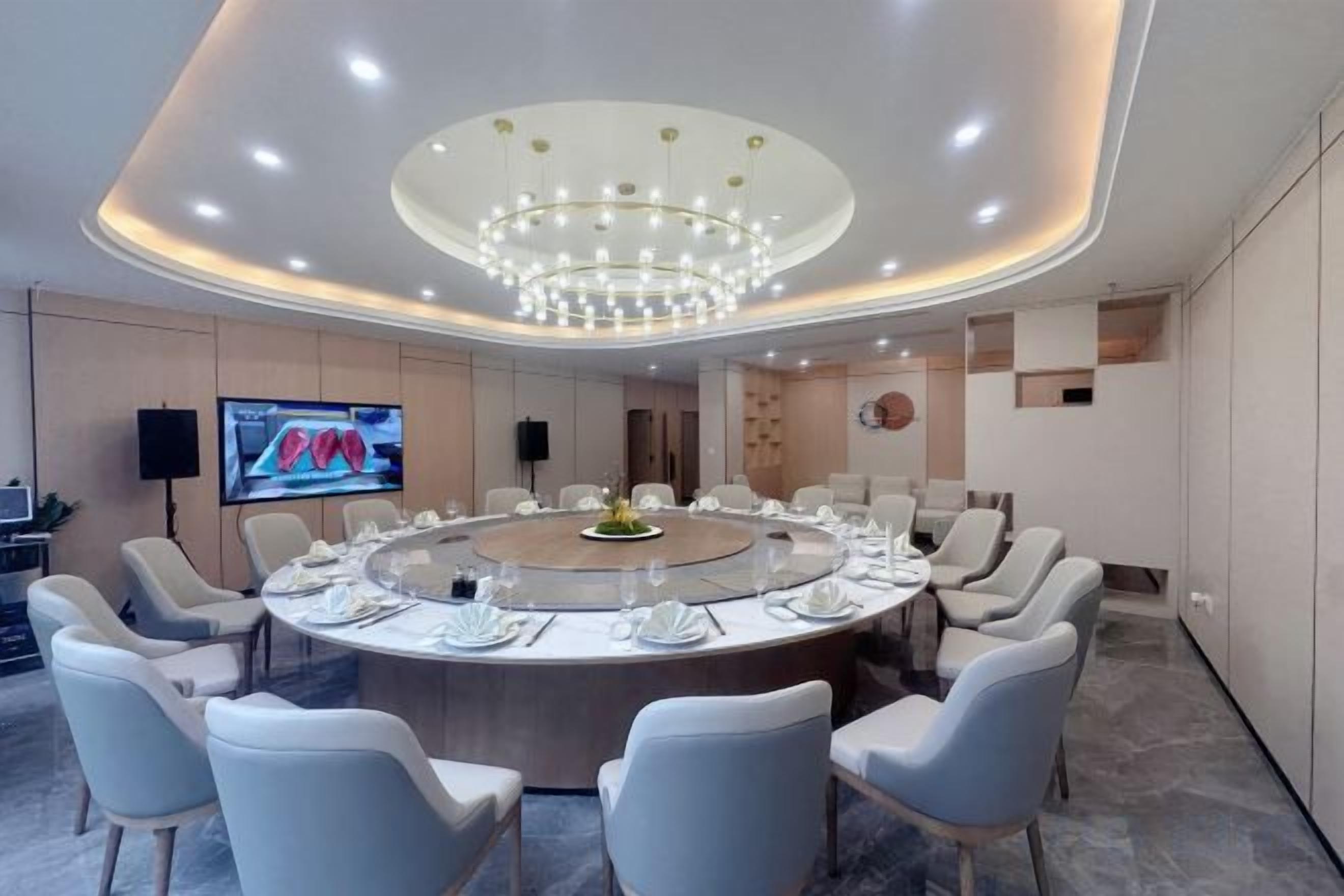 A conference room with a round table, chairs, a large chandelier, and a television screen.