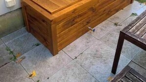 Un banco de madera con estructura metálica, ubicado al aire libre junto a una pared de edificio.