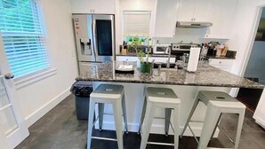 Una cocina moderna con encimera de granito, electrodomésticos de acero inoxidable y tres taburetes de bar.