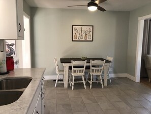 A kitchen with a dining table and chairs, a ceiling fan, and a framed artwork on the wall.