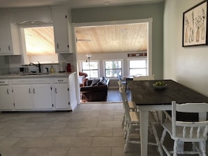 A spacious kitchen with white cabinets, a dining table with white chairs, and a view of the living area through large windows.