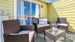 Une terrasse dotée de meubles en osier, d’une table en verre et offrant une vue sur un bâtiment dont le revêtement extérieur est jaune.