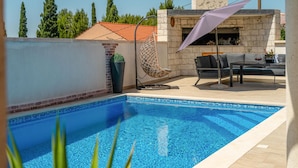 Una piscina con bordo piastrellato, una sedia a dondolo, un tavolo con posti a sedere all'aperto e un camino in pietra.