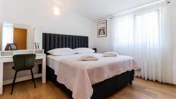 A bedroom with a bed, a desk, a chair, and a window with curtains. - Beach front apartment in Solin (Solin)