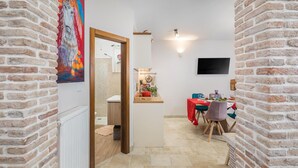 Un pasillo estrecho que desemboca en una zona de comedor, con una mesa dispuesta para dos personas, sillas, un televisor de pantalla plana en la pared y un cuadro en la pared izquierda.