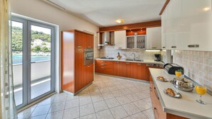 Une cuisine moderne avec des meubles en bois, une cuisinière à gaz et une vue sur une piscine, visible à travers une porte-fenêtre coulissante.
