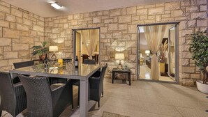 Un coin repas avec un mur en pierre, une table en verre, des chaises en osier et un miroir.