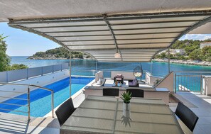 Ein Poolbereich mit überdachter Sitzgelegenheit, einem kleinen Pool und Blick auf das Meer sowie eine felsige Küstenlinie.
