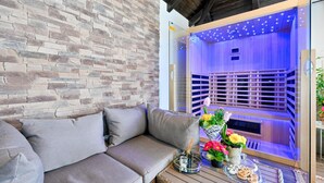 Un espace extérieur accueillant, avec un mur en pierre, un canapé confortable et une table sur laquelle sont disposés un plateau de collations et un bouquet de fleurs.
