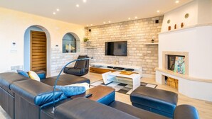 A modern living room with a stone wall, a fireplace, a flat-screen TV, and a sofa.