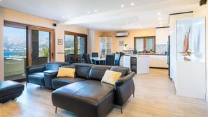 A modern living room with a leather sofa, dining area, kitchen, and a view of the sea.