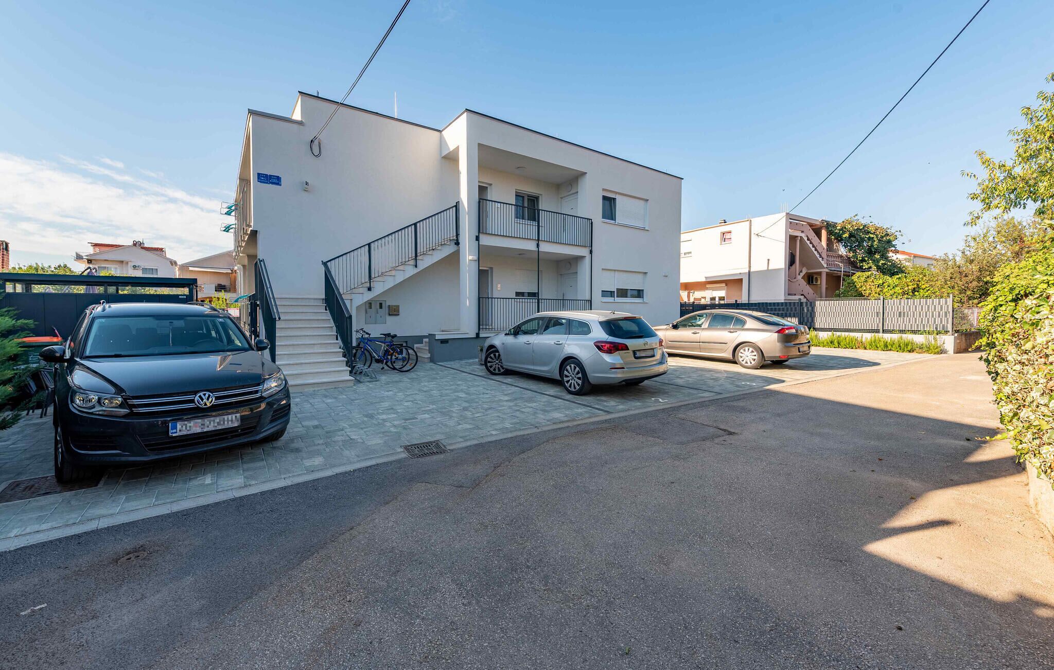 Un bâtiment moderne avec un escalier, deux voitures garées et un vélo.