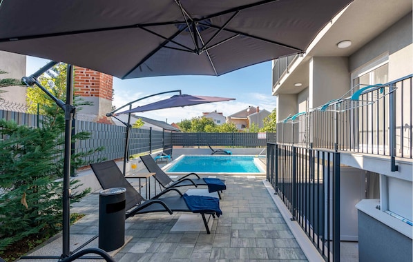 A swimming pool with lounge chairs and a covered area, surrounded by a fence and buildings. - Awesome apartment in Zadar with swimming pool (Zadar)