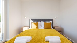 Ein ordentlich bezogenes Bett mit gelber Bettdecke, zwei weißen Handtüchern und einem grauen Kopfteil.