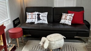 A modern living room with a black leather sofa, red and white dog-themed cushions, a small white dog figurine, a red stool, and a clear glass coffee table. - "Woof"  Lodge  minutes from the Beach and Redwoods (Crescent City)