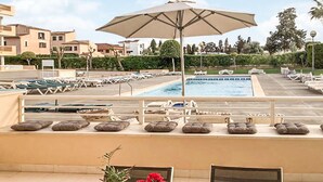 Un espace aménagé au bord de la piscine, avec des chaises longues et des parasols, une piscine, et une vue sur les bâtiments et la végétation environnants.