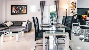 Un salon moderne avec une table à manger en verre, des fauteuils en cuir noir, un canapé et un grand tableau abstrait.