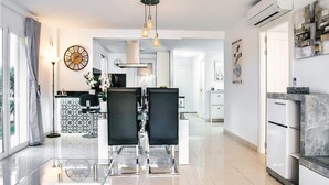 Une cuisine moderne avec un coin repas, agrémentée d’une grande horloge, de luminaires suspendus et offrant une vue sur l’extérieur.