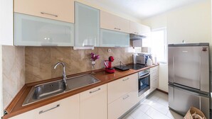 A modern kitchen with a stainless steel sink, a built-in oven, a refrigerator, and a coffee maker on the countertop. - Nice home in Okrug Gornji with sauna (Okrug Gornji)