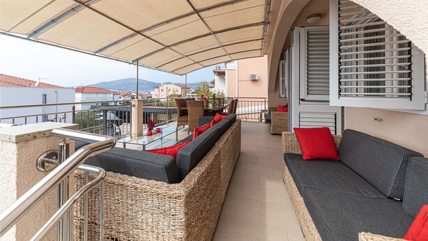 A covered outdoor seating area with wicker furniture and a cushioned sofa, overlooking a cityscape with buildings and a mountain in the distance. - Nice home in Okrug Gornji with sauna (Okrug Gornji)