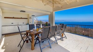 Ruokailutila, jossa on pöytä ja tuolit, taustalla keittiö ja näkymä merelle.