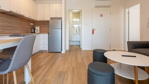 Een moderne keuken met witte kasten, een roestvrijstalen koelkast en een houten aanrecht. Er is een eethoek met een tafel en stoelen, en een kleine ronde tafel met een afstandsbediening erop.