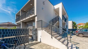 Een modern, tweelaags gebouw met een balkon op de bovenverdieping, een hekwerk en een trap naar de ingang.