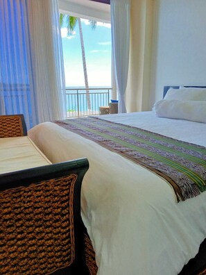 Relax in a spacious room with a large bed, wicker chair, and ocean views from the balcony.