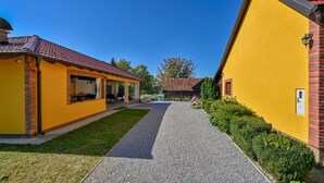 A yellow building with a red-tiled roof, a gravel pathway, and a small garden area. - Cozy home in Gornja Ploscica (Gornja Ploscica)
