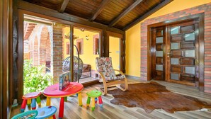 A cozy room with a wooden ceiling, a brick wall, a large window, a chair, a rug, and children's stools. - Cozy home in Gornja Ploscica (Gornja Ploscica)