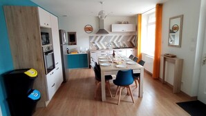 A modern kitchen with a dining area, wooden cabinets, and a black trash bin.