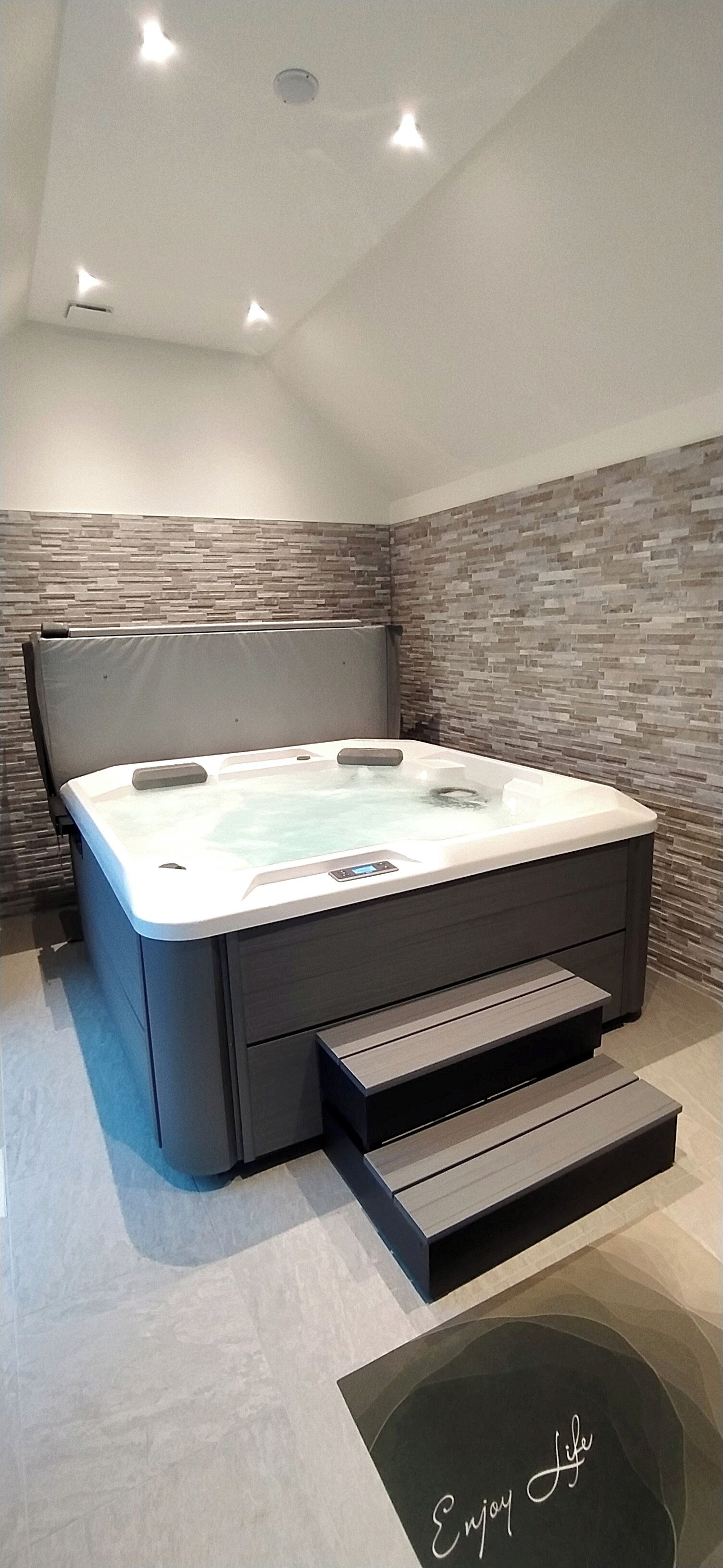 A modern bedroom with a built-in hot tub, a headboard, and a stone-patterned wall.