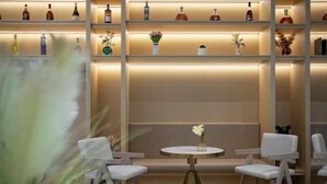 A modern interior with a bar area featuring shelves of bottles and vases, two white chairs, and a round table with a vase of flowers. - Hangzhou Dingqiao Kaiyuan Yiju Hotel (Hangzhou)