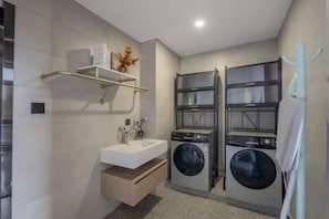A modern bathroom with a built-in washing machine, a sink, and a shelf with toiletries. - Hangzhou Dingqiao Kaiyuan Yiju Hotel (Hangzhou)