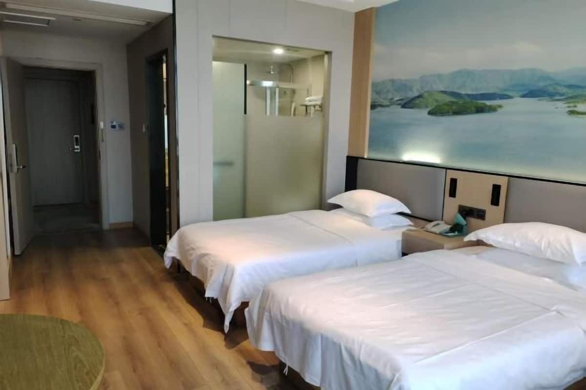 Ein Hotelzimmer mit zwei Betten, einem Landschaftsbild und einer Glastrennwand.