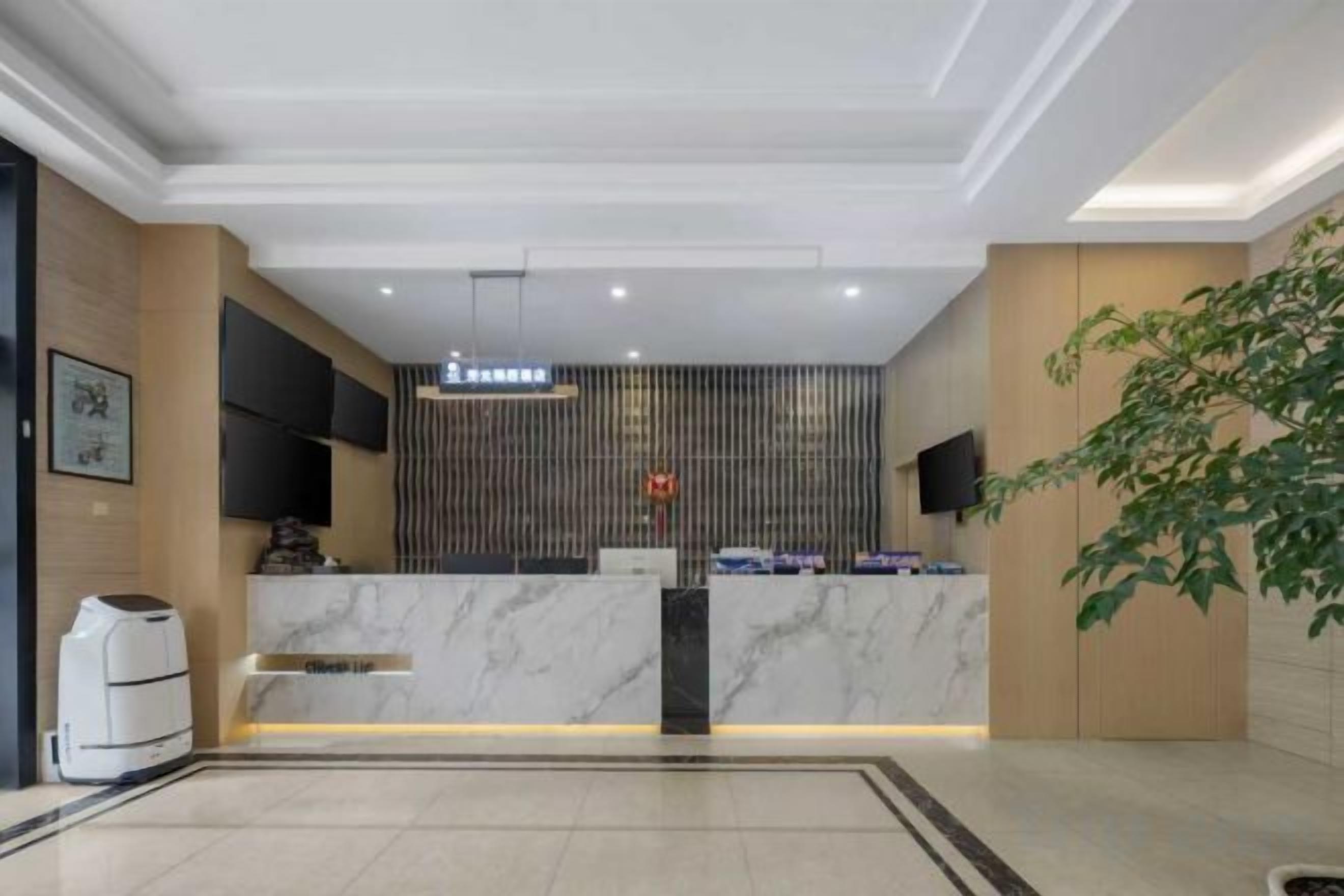 A hotel reception area with a marble counter, a flat-screen TV, and a potted plant.