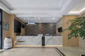 A hotel reception area with a marble counter, a flat-screen TV, and a potted plant. - Hangzhou Dingqiao Kaiyuan Yiju Hotel (Hangzhou)