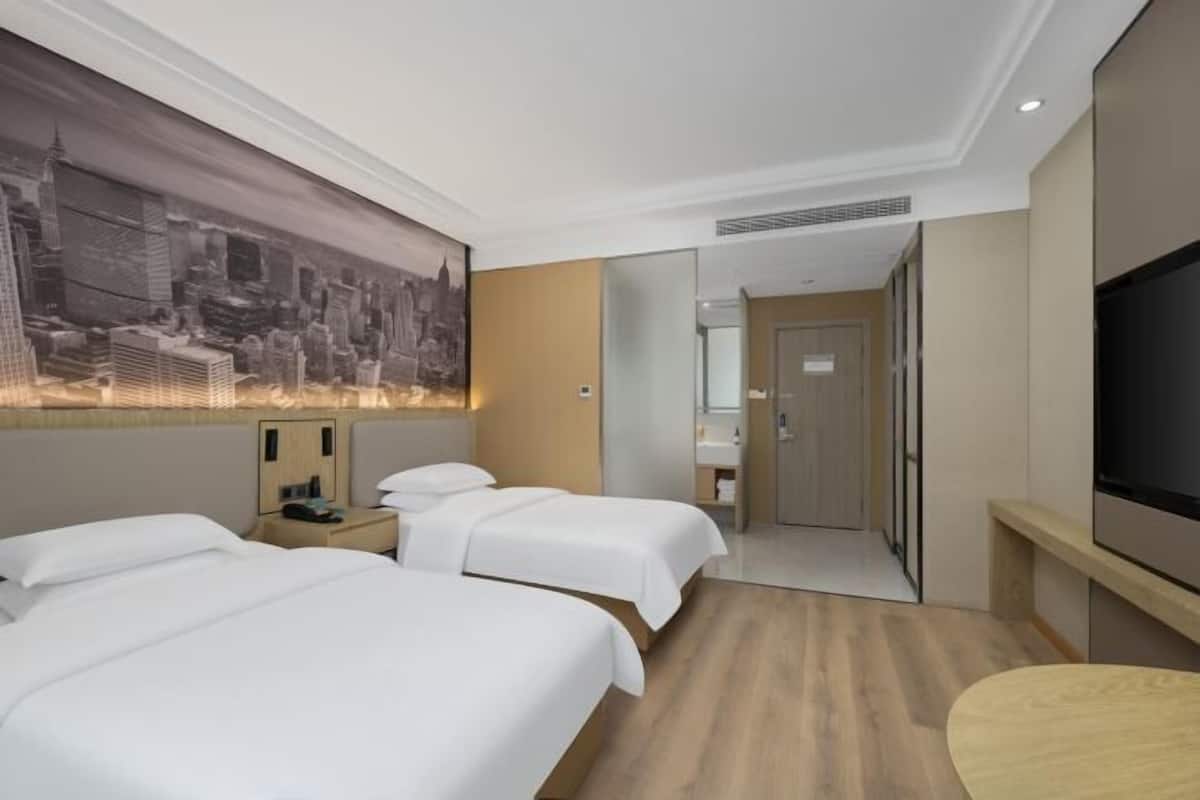 Ein Hotelzimmer mit zwei Betten, einem großen Stadtbild, einem Fernseher und einem Spiegel.