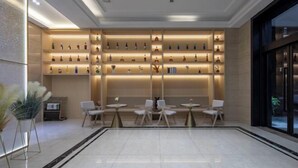 A modern hotel lobby with a central seating area, a wall of illuminated shelves displaying various items, and a large window providing a view of the outside. - Hangzhou Dingqiao Kaiyuan Yiju Hotel (Hangzhou)