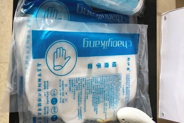 Un sac en plastique avec une étiquette bleue et du texte dans une langue étrangère, placé sur une surface à côté d’un objet blanc.