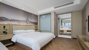 A modern hotel room with a large bed, a nightstand, a bedside table, a wall-mounted TV, and a bathroom visible through an open door. - Hangzhou Dingqiao Kaiyuan Yiju Hotel (Hangzhou)