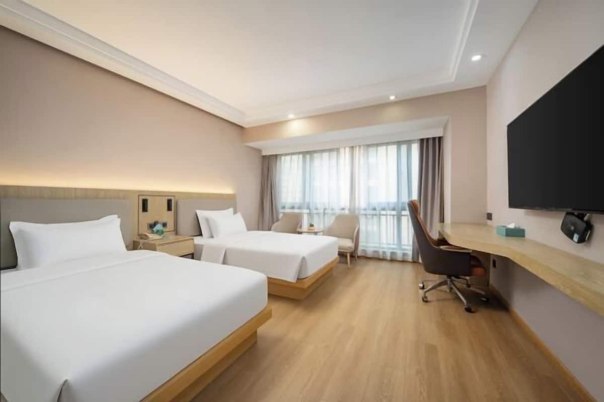 Ein Hotelzimmer mit zwei Betten, einem Schreibtisch, einem Stuhl, einem Fernseher und einem Fenster mit Vorhängen.