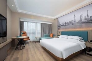 Une chambre d’hôtel moderne avec un grand lit, un bureau avec une chaise, une petite table et un tableau représentant un paysage urbain accroché au mur.