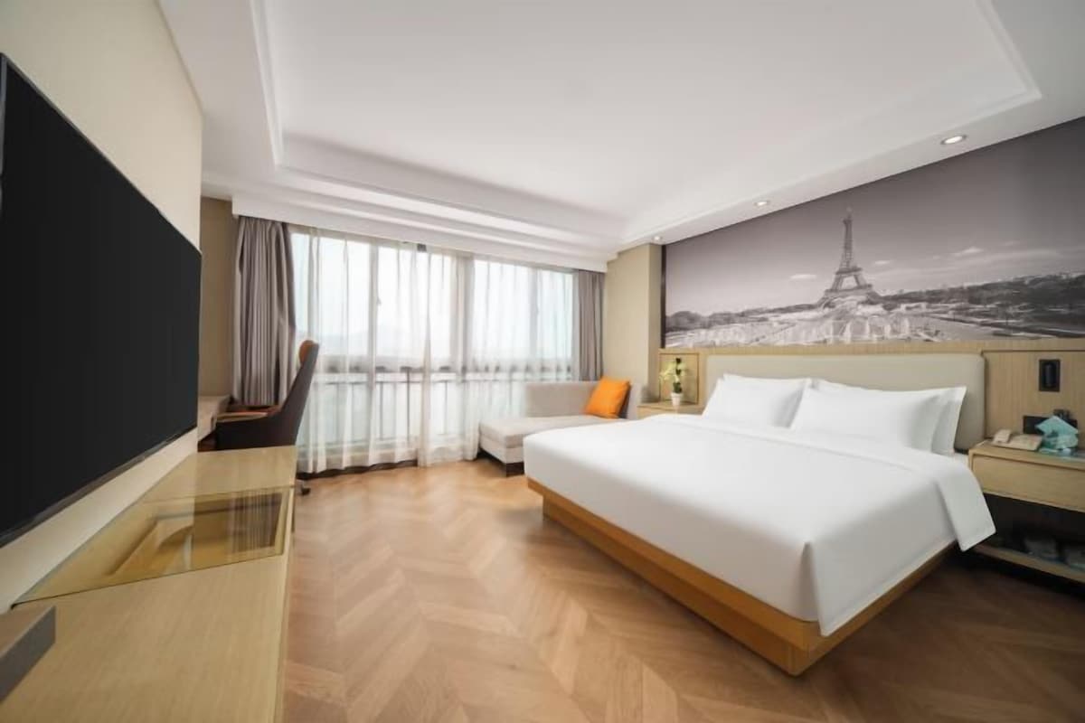 Una habitación de hotel con cama, escritorio, silla, televisor y un amplio ventanal.