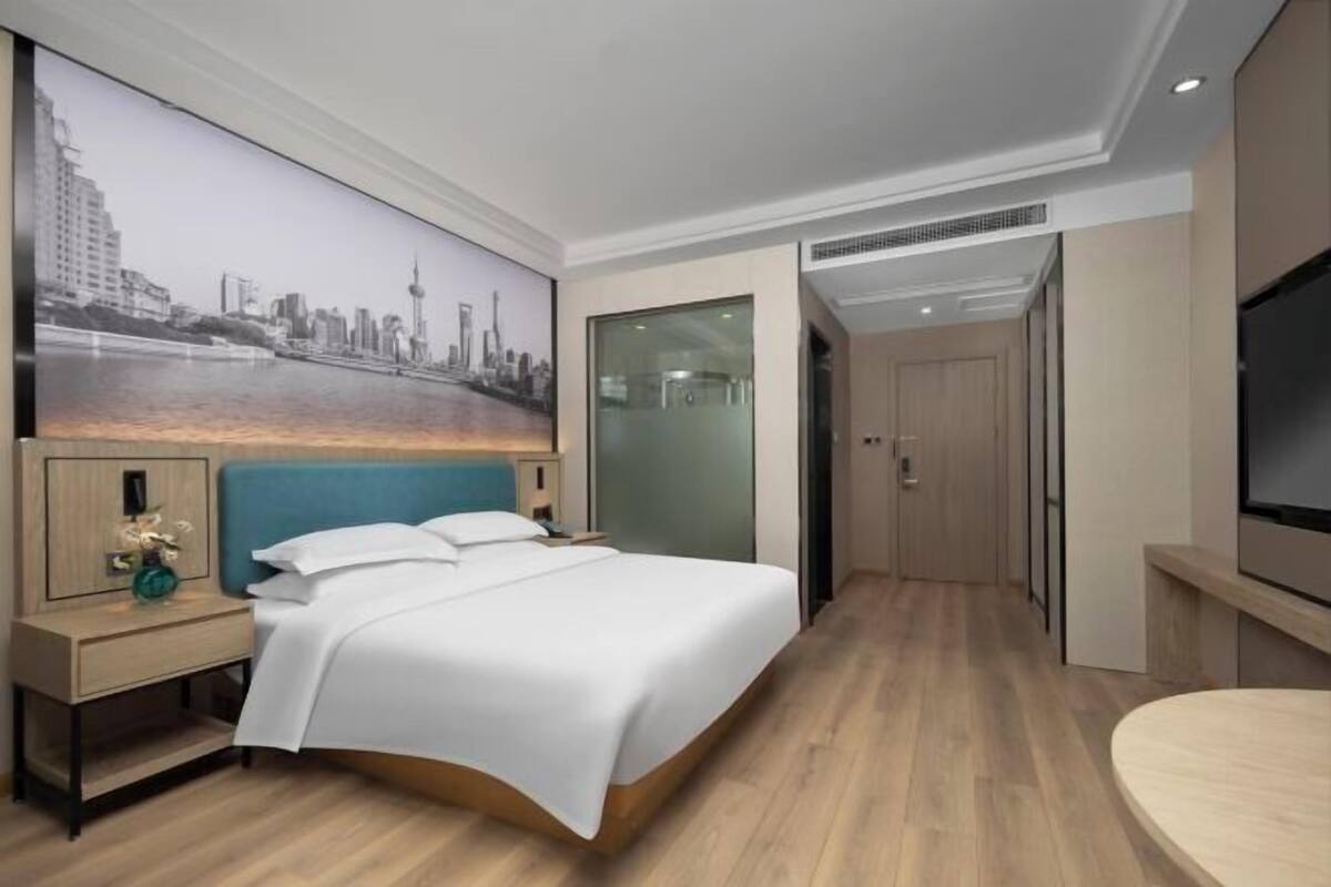 Ein modernes Hotelzimmer mit einem großen Bett, einem Nachttisch, einem Fernseher und einem Stadtbild an der Wand.