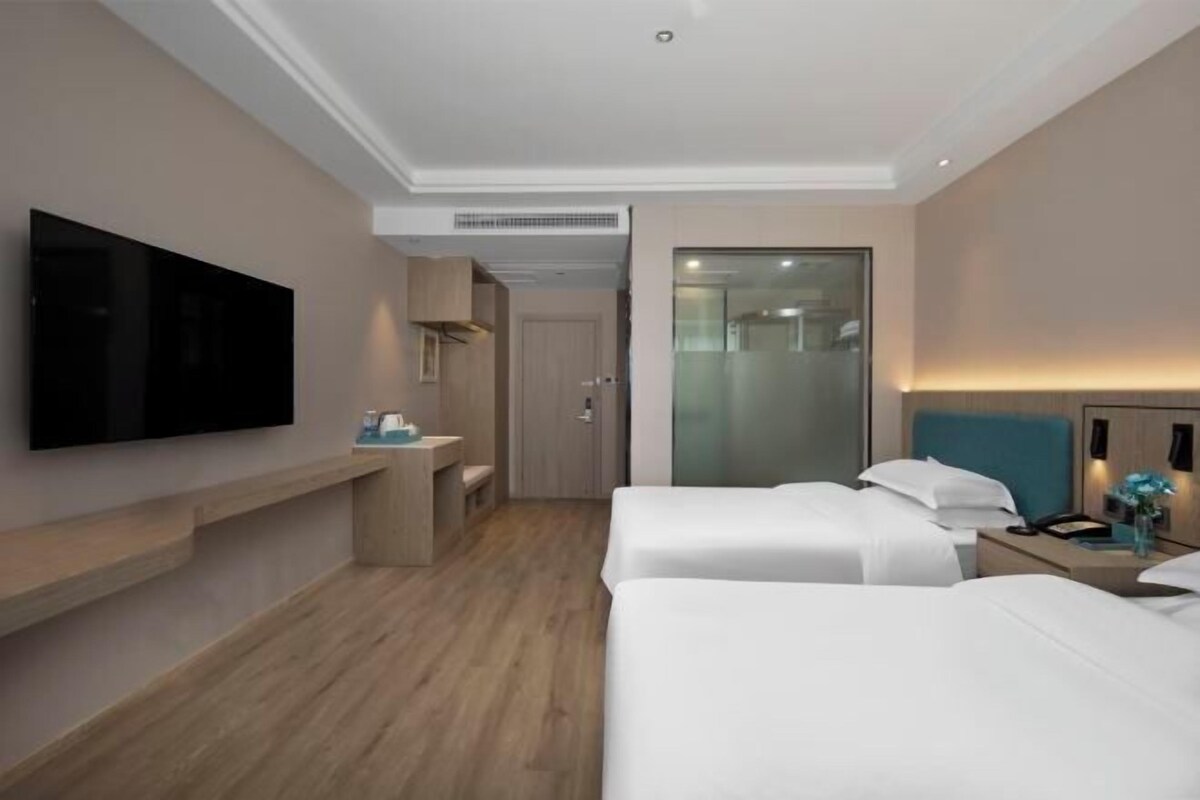Une chambre d’hôtel avec deux lits, un téléviseur à écran plat fixé au mur, une table de chevet avec une lampe et un miroir.