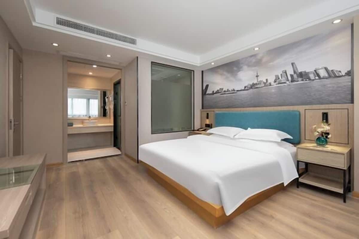 Ein modernes Hotelzimmer mit einem großen Bett, einem Stadtbild-Wandgemälde, einem begehbaren Kleiderschrank und einer Duschkabine aus Glas.