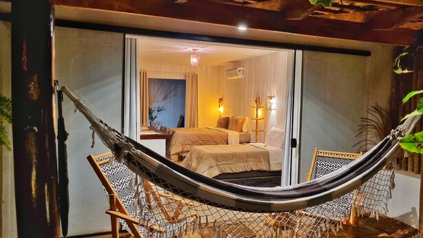 A hammock chair and a small table in a room with a bed and a nightstand. - Morada dos Saguis Chalés (Alto Paraíso de Goiás)