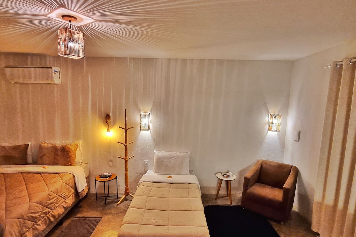 Ein Hotelzimmer mit Bett, Sofa, Sessel, kleinem Tisch, Kleiderständer und zwei Wandleuchten.