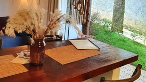 A dining area with a wooden table, a vase with dried plants, and a view of a garden through a glass door. - Morada dos Saguis Chalés (Alto Paraíso de Goiás)